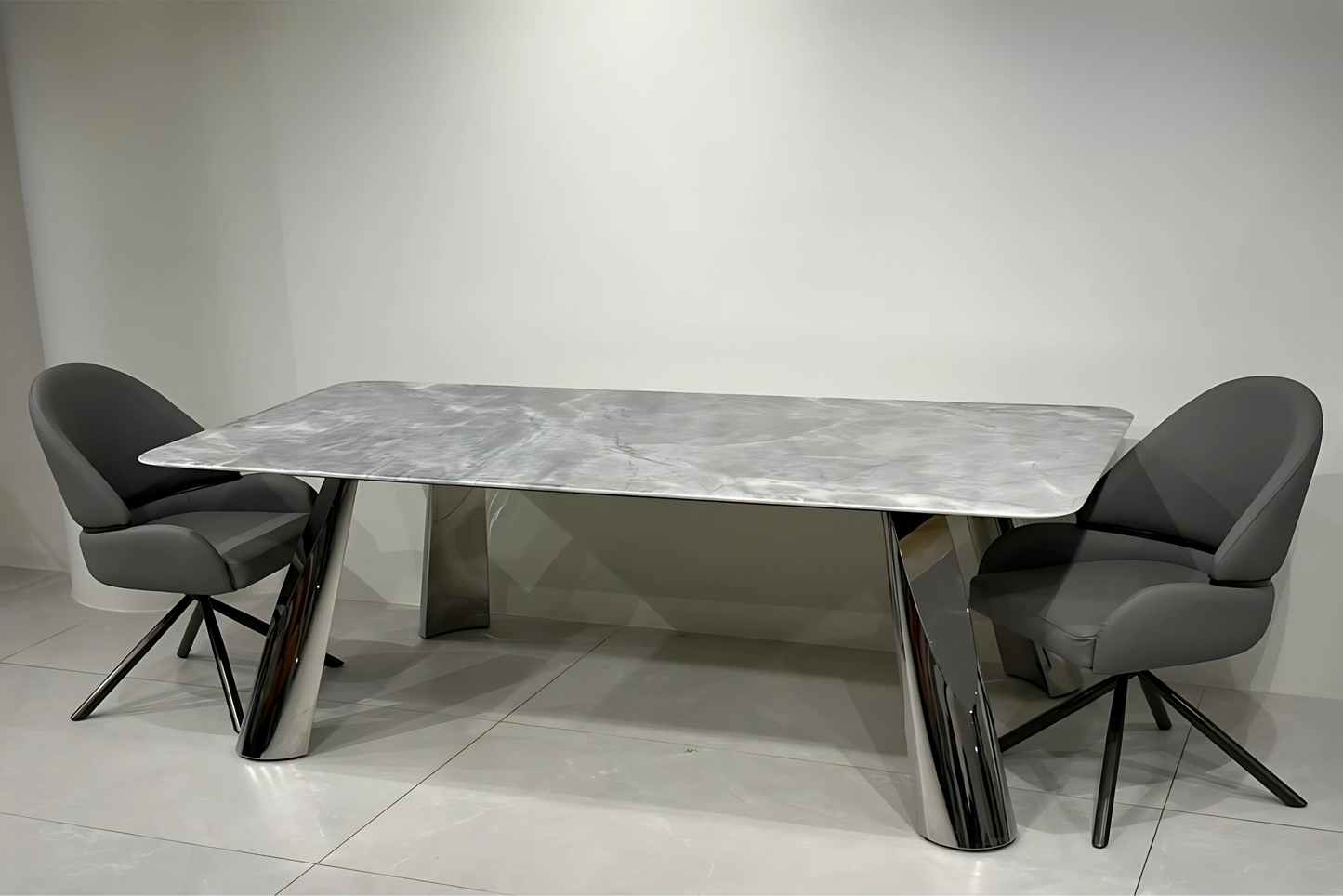 Grey marble dining table with chrome pedestal legs and charcoal swivel dining chairs in modern luxury style.