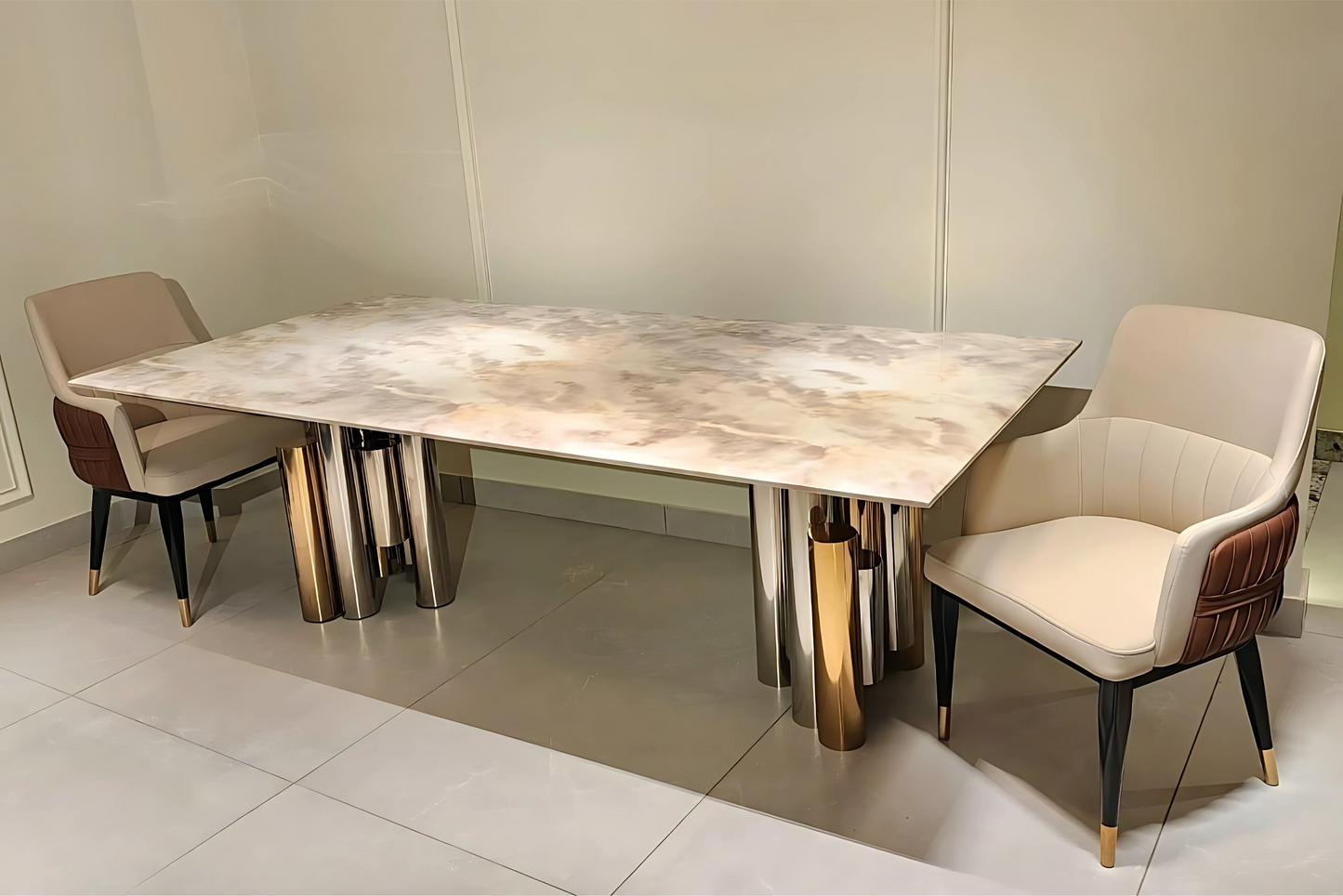 A modern dining table with a marble top and gold and silver colored metal legs, accompanied by two upholstered chairs with beige and brown seats.