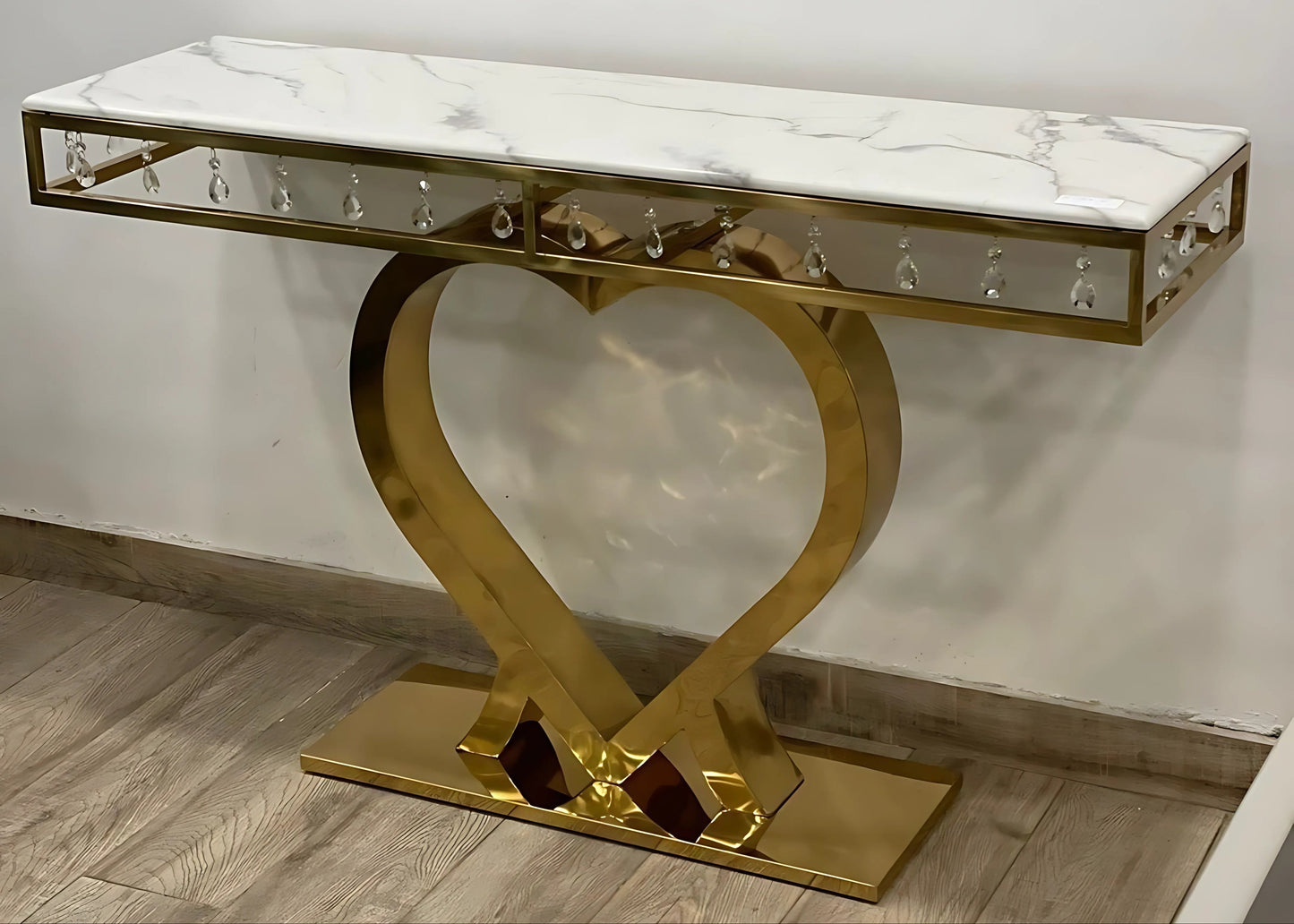 A black marble console table with gold looped legs positioned on a floor against a wall.