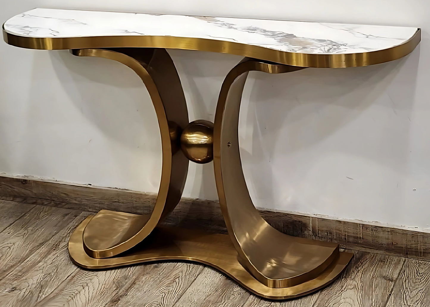 A striking white marble console table with gold looped legs positioned on a wooden floor against a white background.