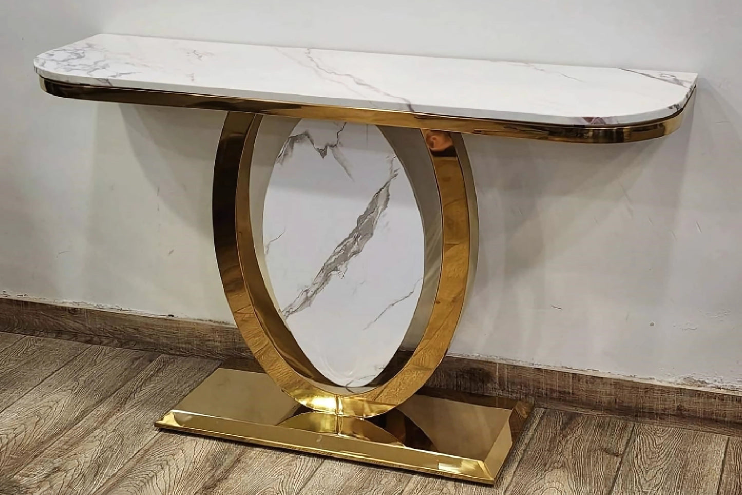 A black marble console table with gold looped legs placed on a wooden floor against a white background.