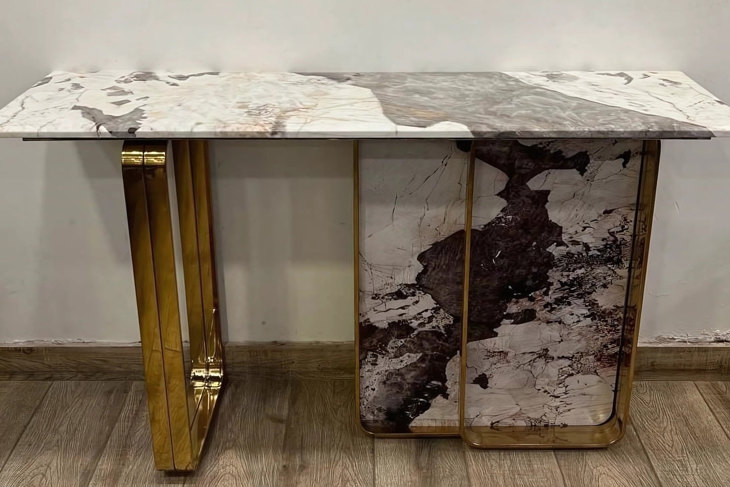 A black marble console table with gold looped legs placed against a wall on a wooden floor.
