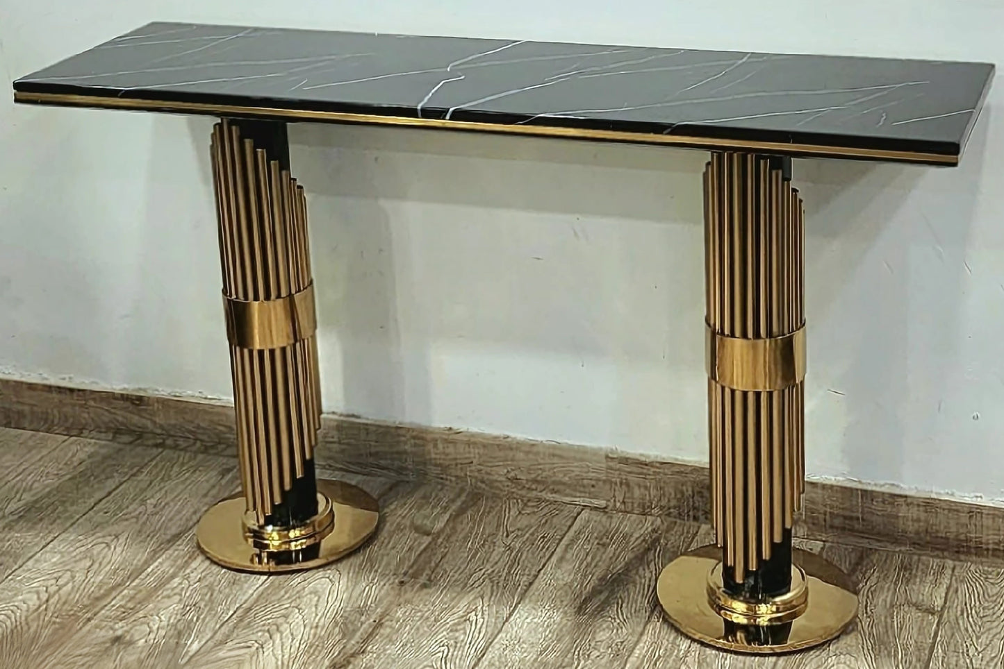 A black marble console table with gold looped legs, placed on a wooden floor against a white background.
