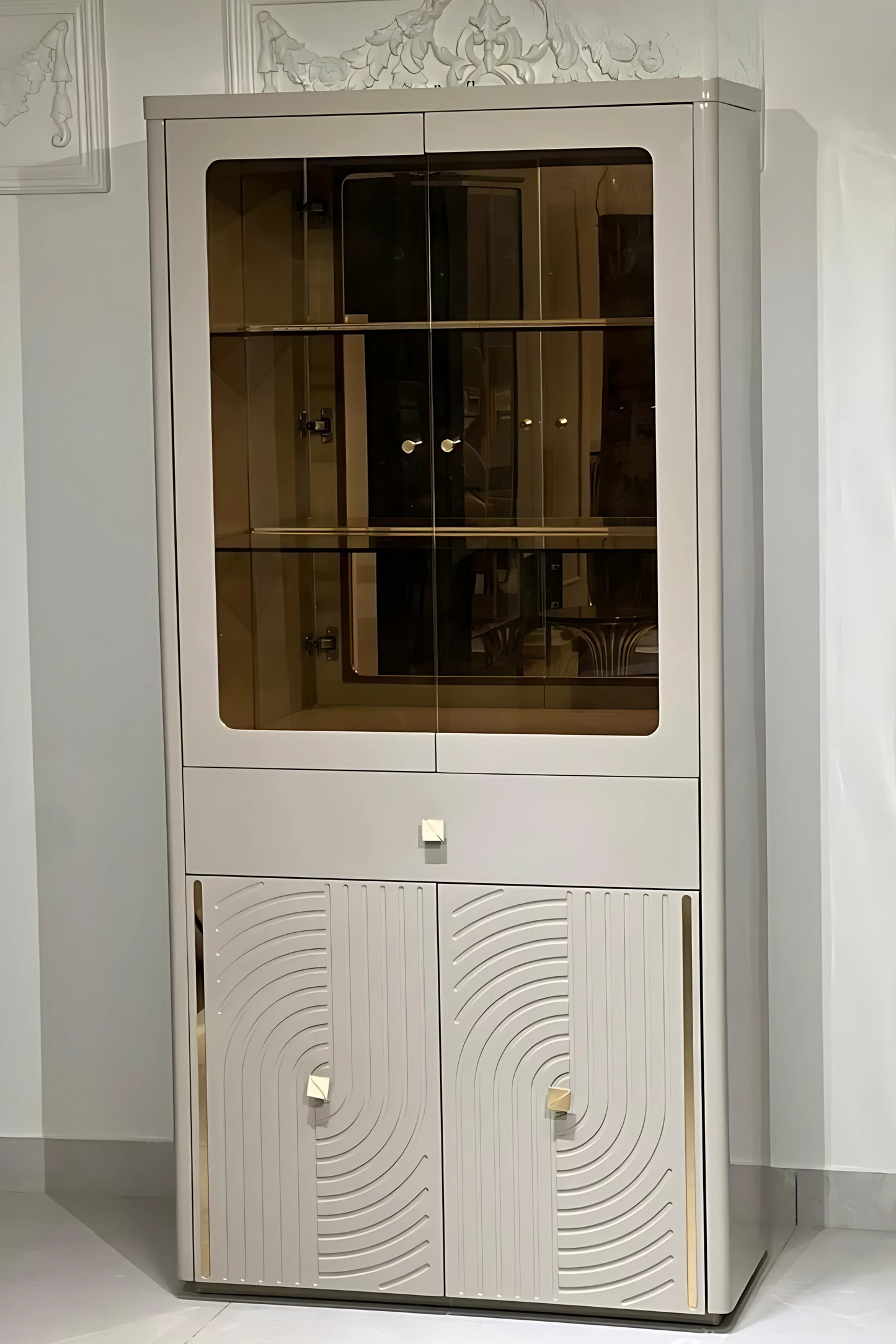 An ivory-colored wooden curio cabinet with a glass panel on the upper part and patterned doors on the lower part, set against a white background.