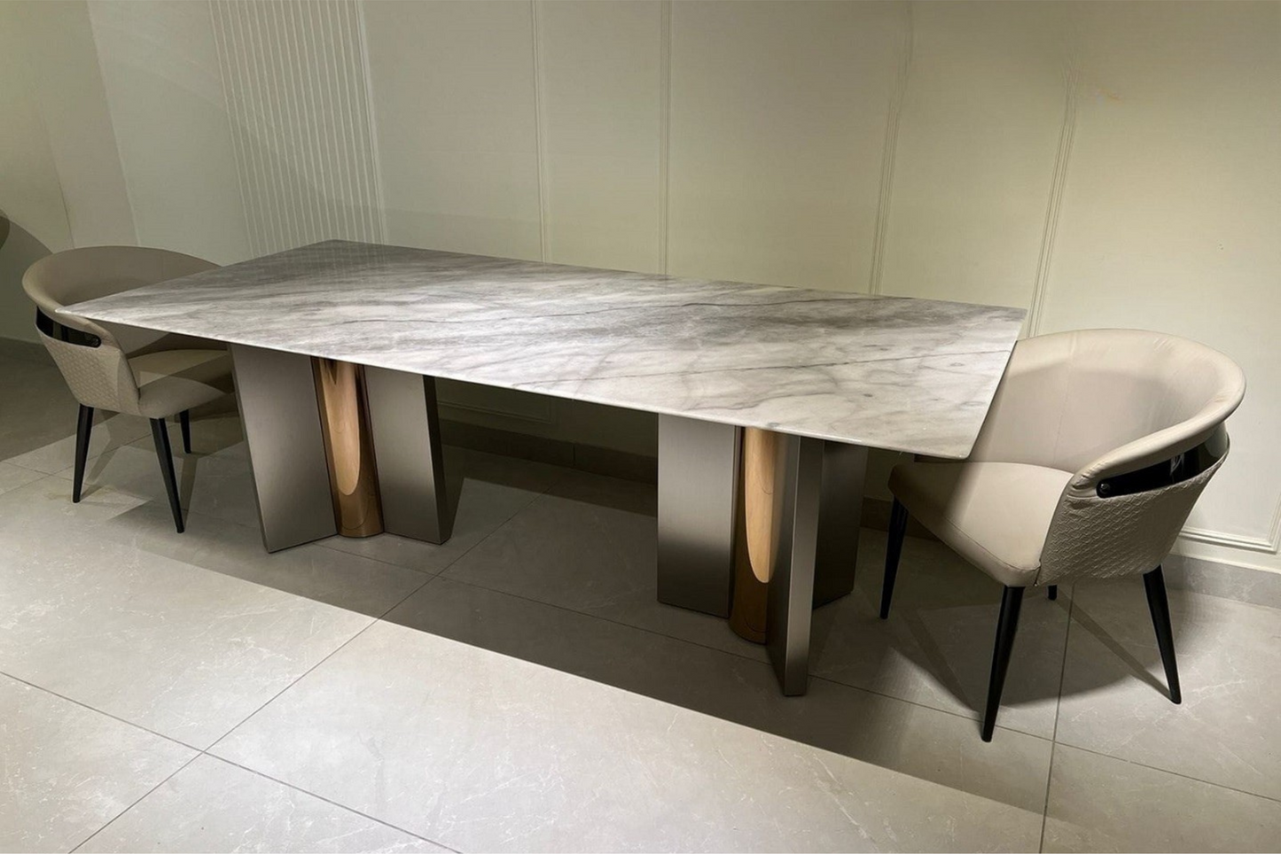 A modern dining table with a marble top flanked by two chairs with upholstered seats.