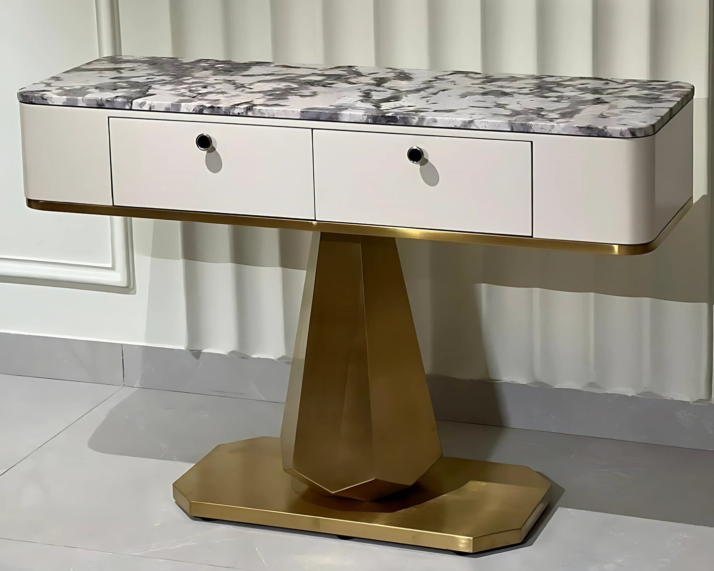 A black marble console table with gold looped legs and three drawers, positioned against a window with white curtains.