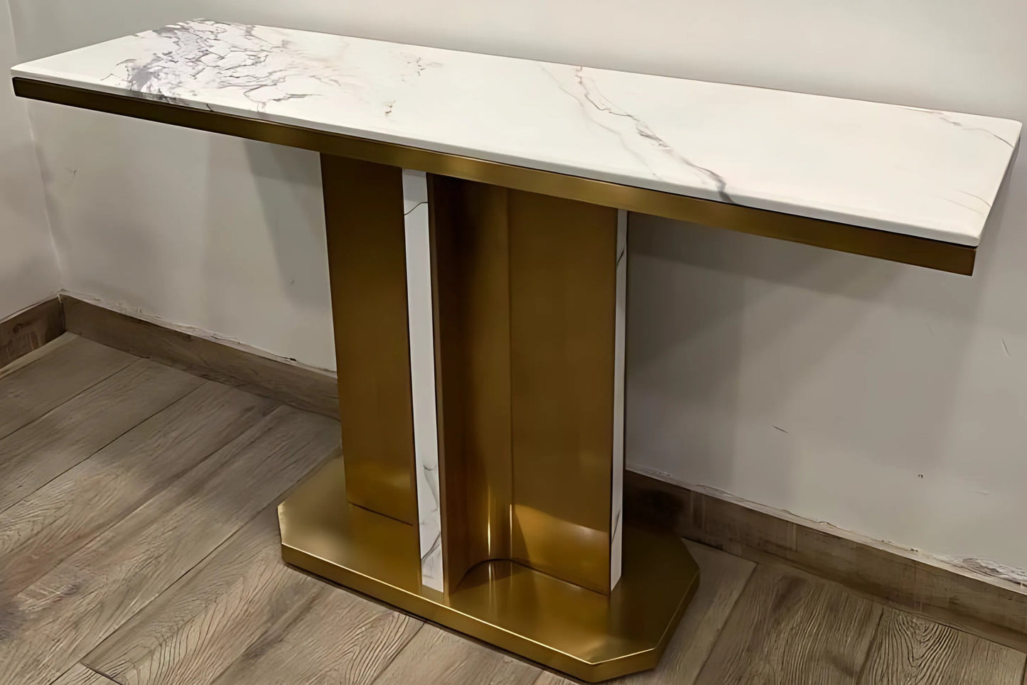 A black marble console table with gold looped legs placed on a wooden floor against a white background.