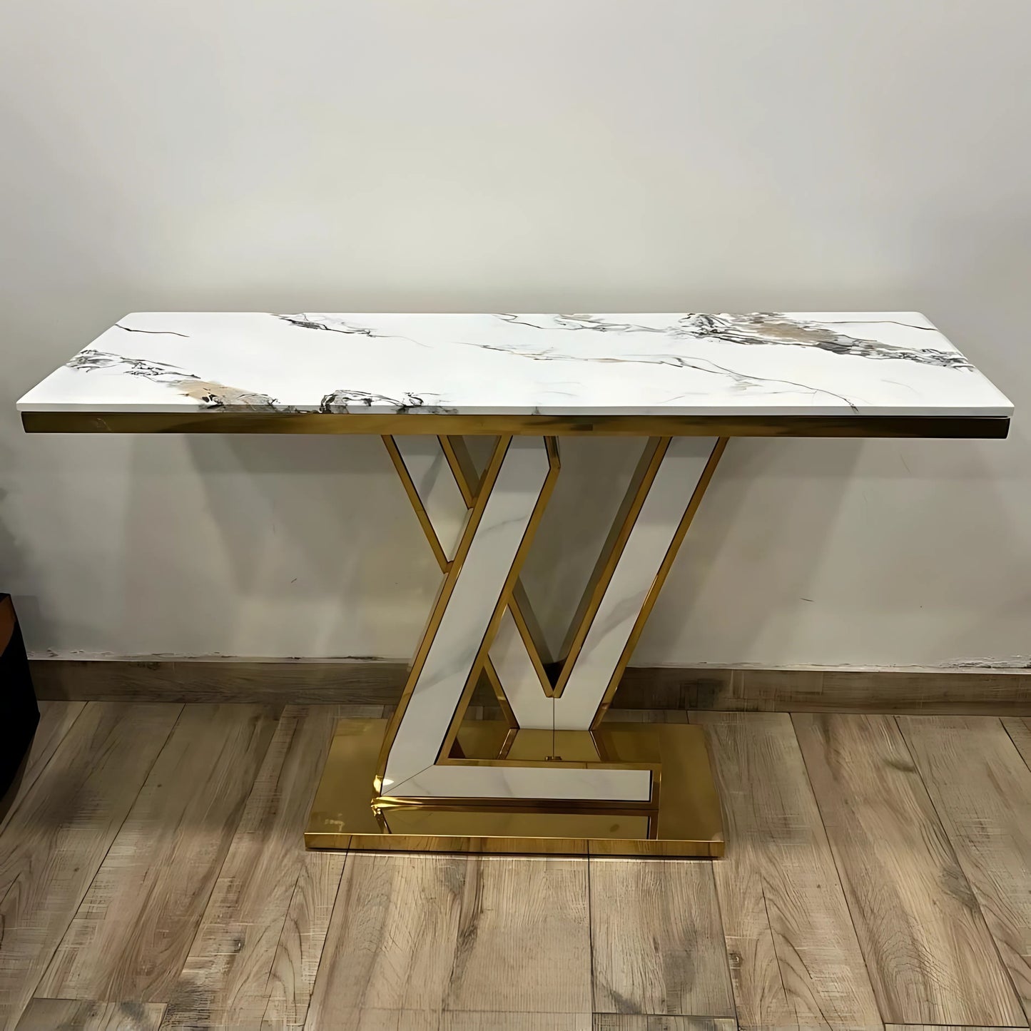 A black marble console table with gold looped legs placed on a wooden floor against a white background.