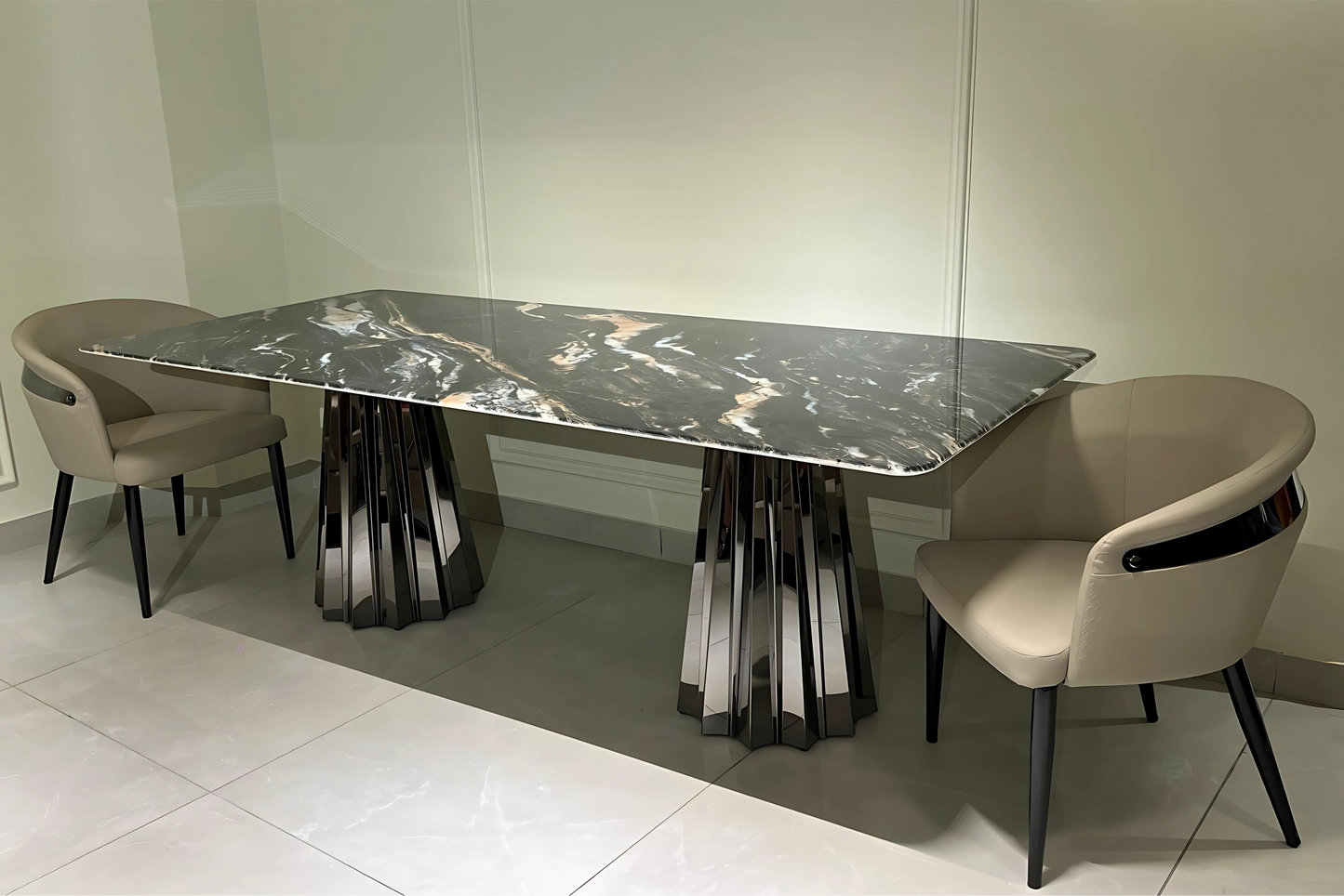 A modern dining table with a dark marble tabletop and metallic legs, flanked by two modern chairs with beige upholstery and dark legs.