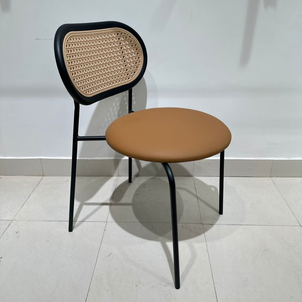Black frame dining chair with woven cane backrest and tan leatherette seat