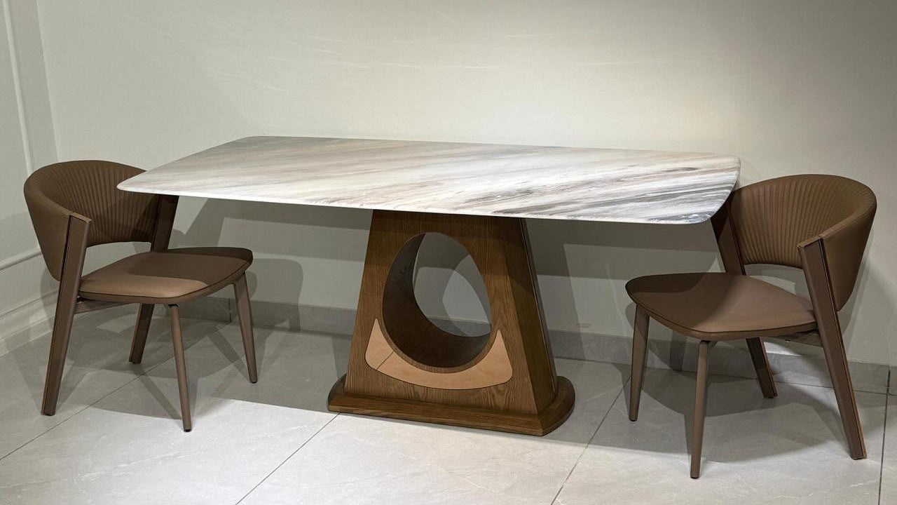 Dining table with marble top and wooden base, accompanied by four chairs on a light-colored floor.