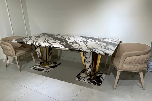 A rectangular dining table with a black and white marble top, gold-colored legs, and surrounded by 2 chairs with beige upholstery.