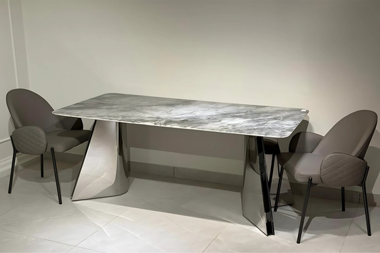 A modern dining table with a gray & white marble-like surface and silver metal legs, flanked by two gray upholstered chairs with black frames.