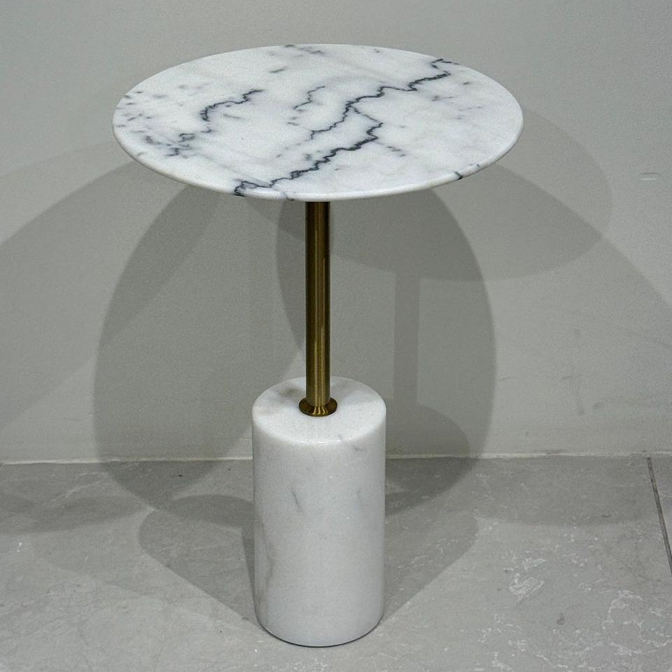 Round marble side table with a gold central column on a gray floor.