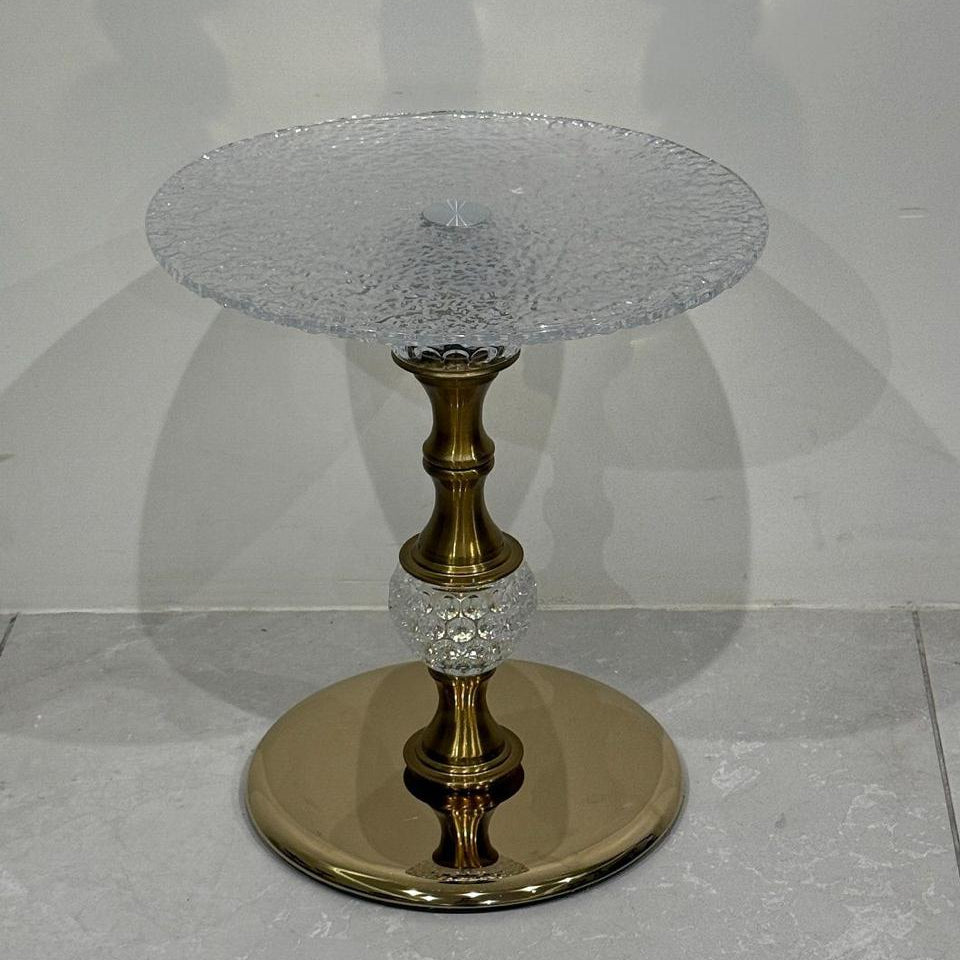 Side table with crystal top and gold base on a light gray background