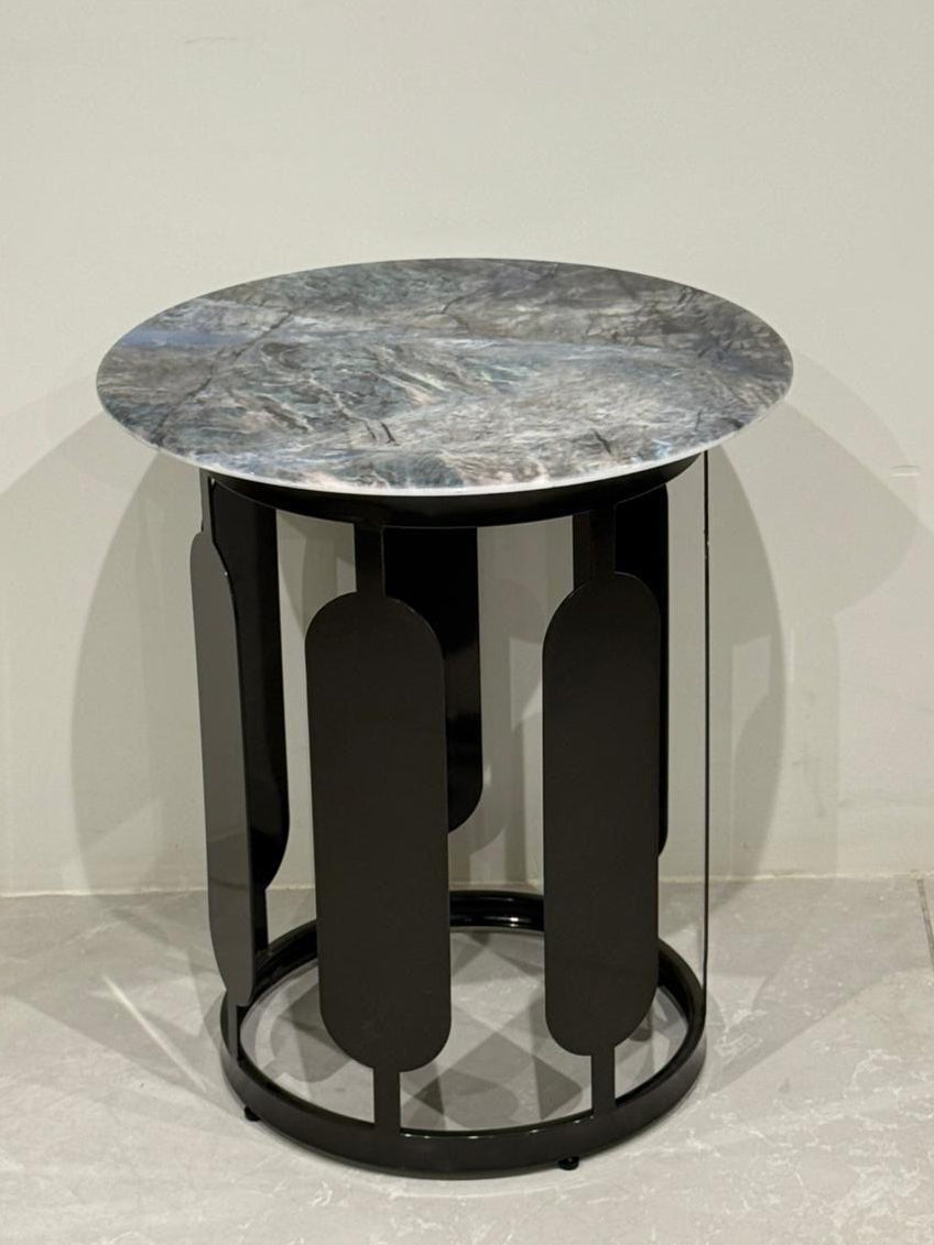 Round side table with marble top and black cylindrical base on a light gray floor.