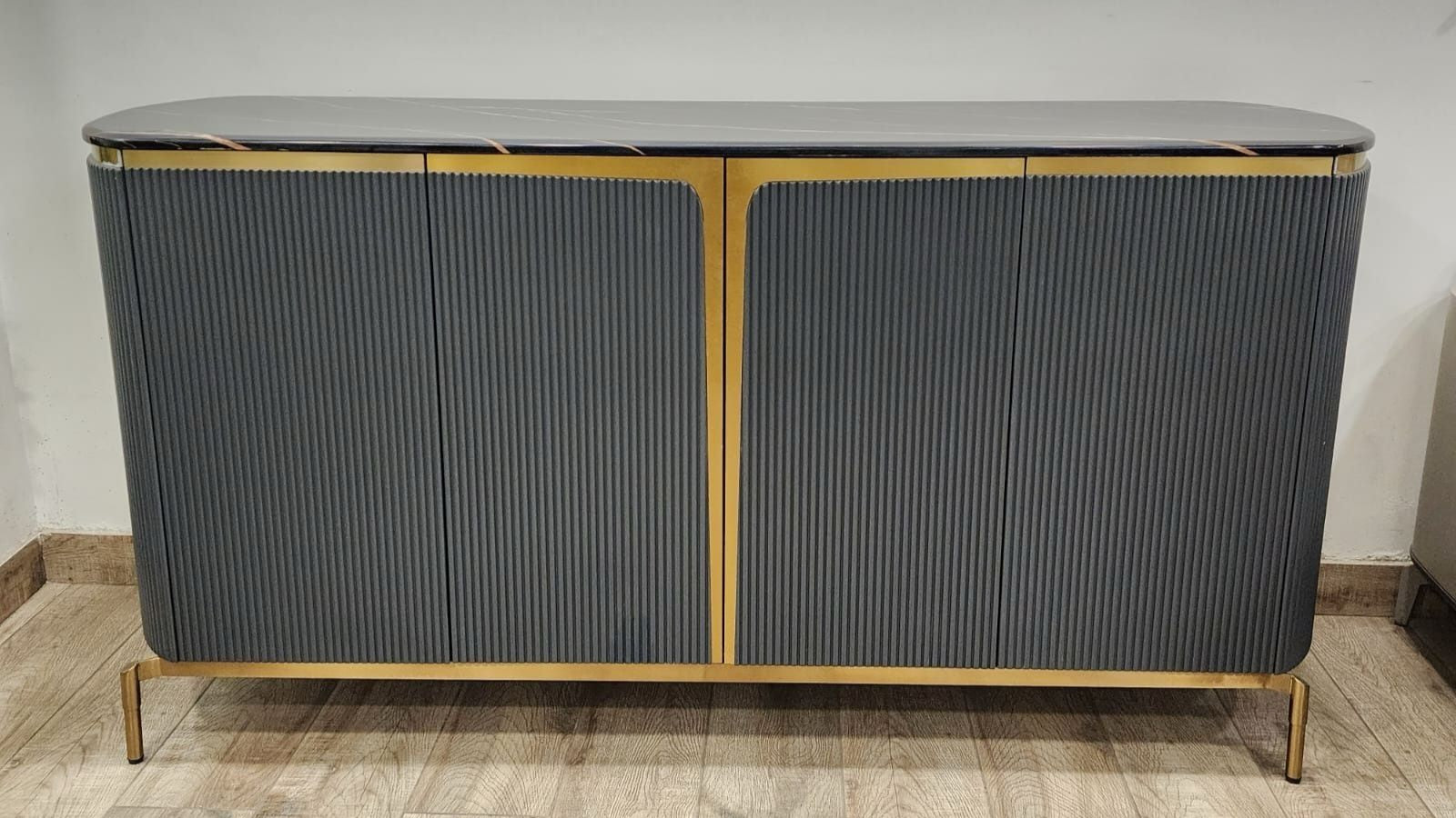Gray sideboard with gold accents on a wooden floor against a white wall.