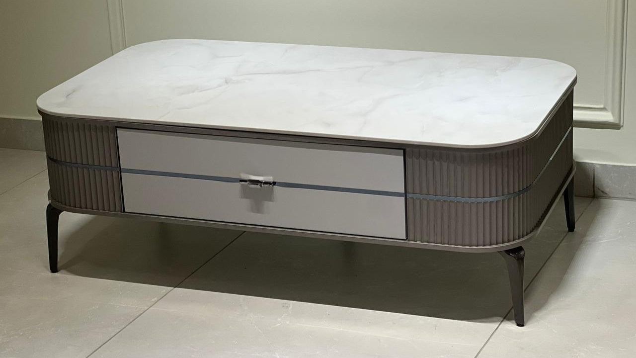 Modern rectangular marble center table with fluted sides, storage drawer, and tapered black legs in a luxury setting