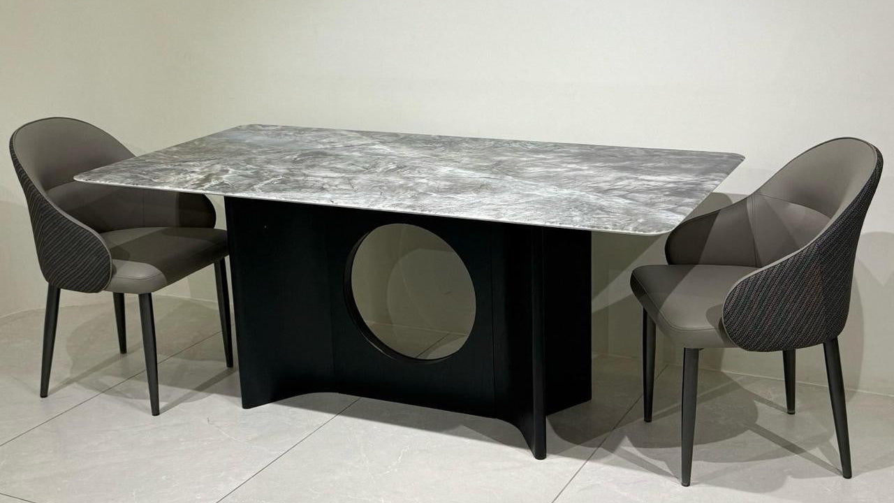 Dining table set with marble-like top and black base, paired with gray chairs on a light background.