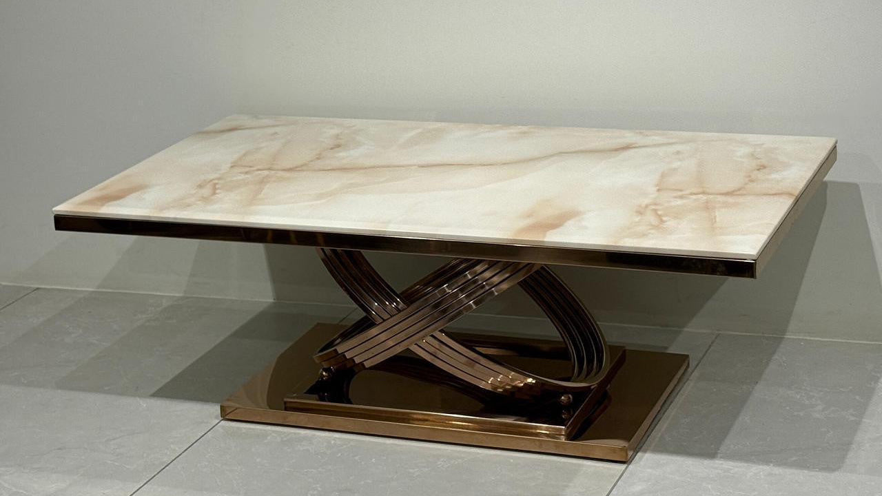 Rose gold center table with marble-like top on a gray floor.