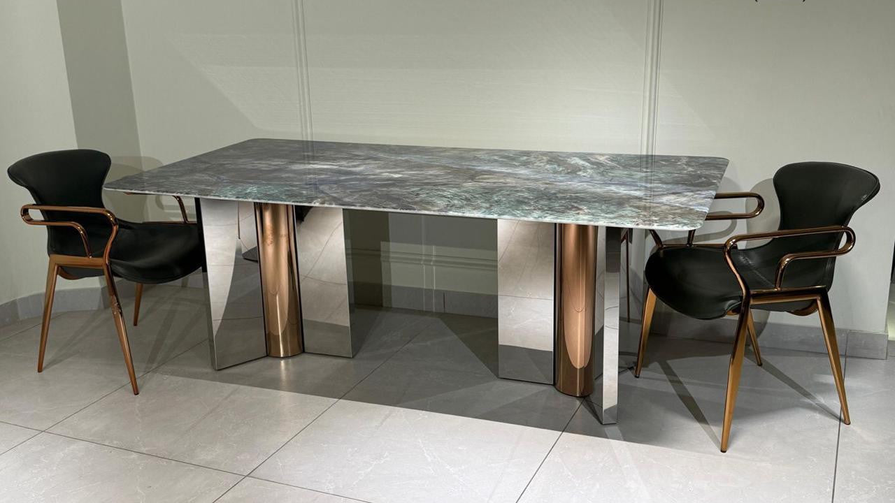 Dining table with marble top and metallic base, accompanied by chairs in a showroom setting. 