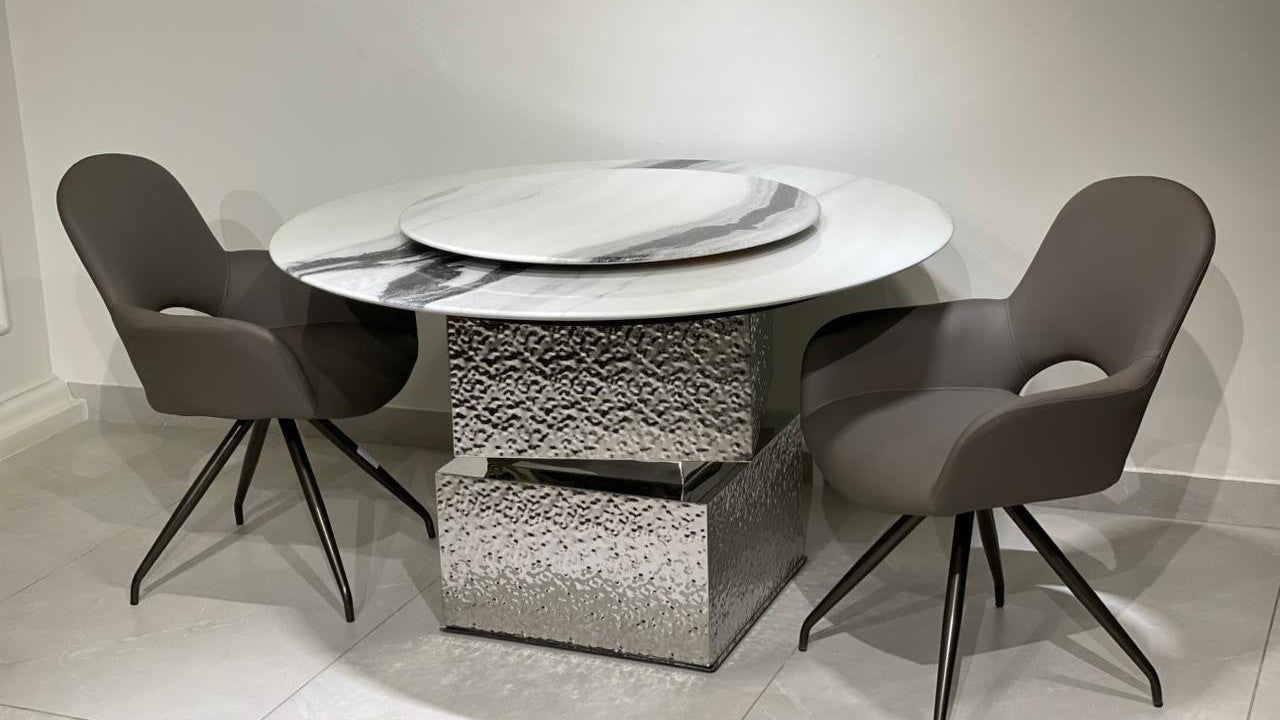 Round marble dining table with textured base and four dark gray chairs in a room. 